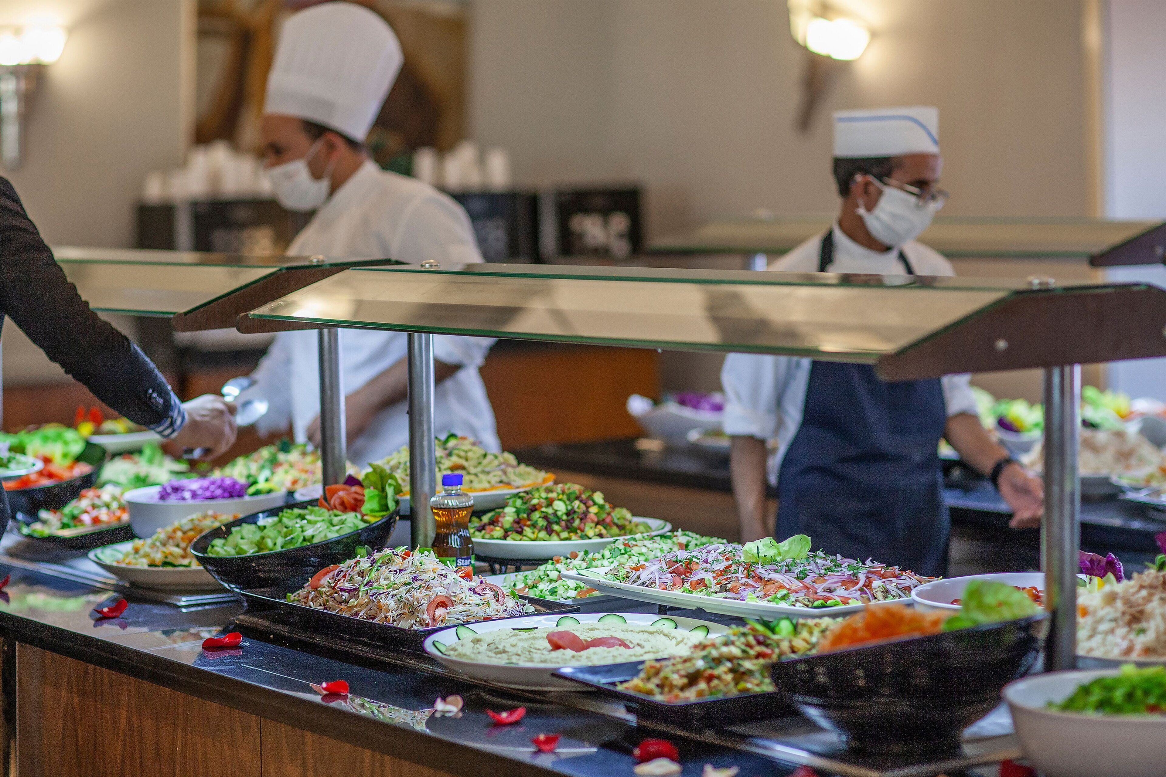 A buffet with various dishes, including salads and other food items, behind a glass partition.