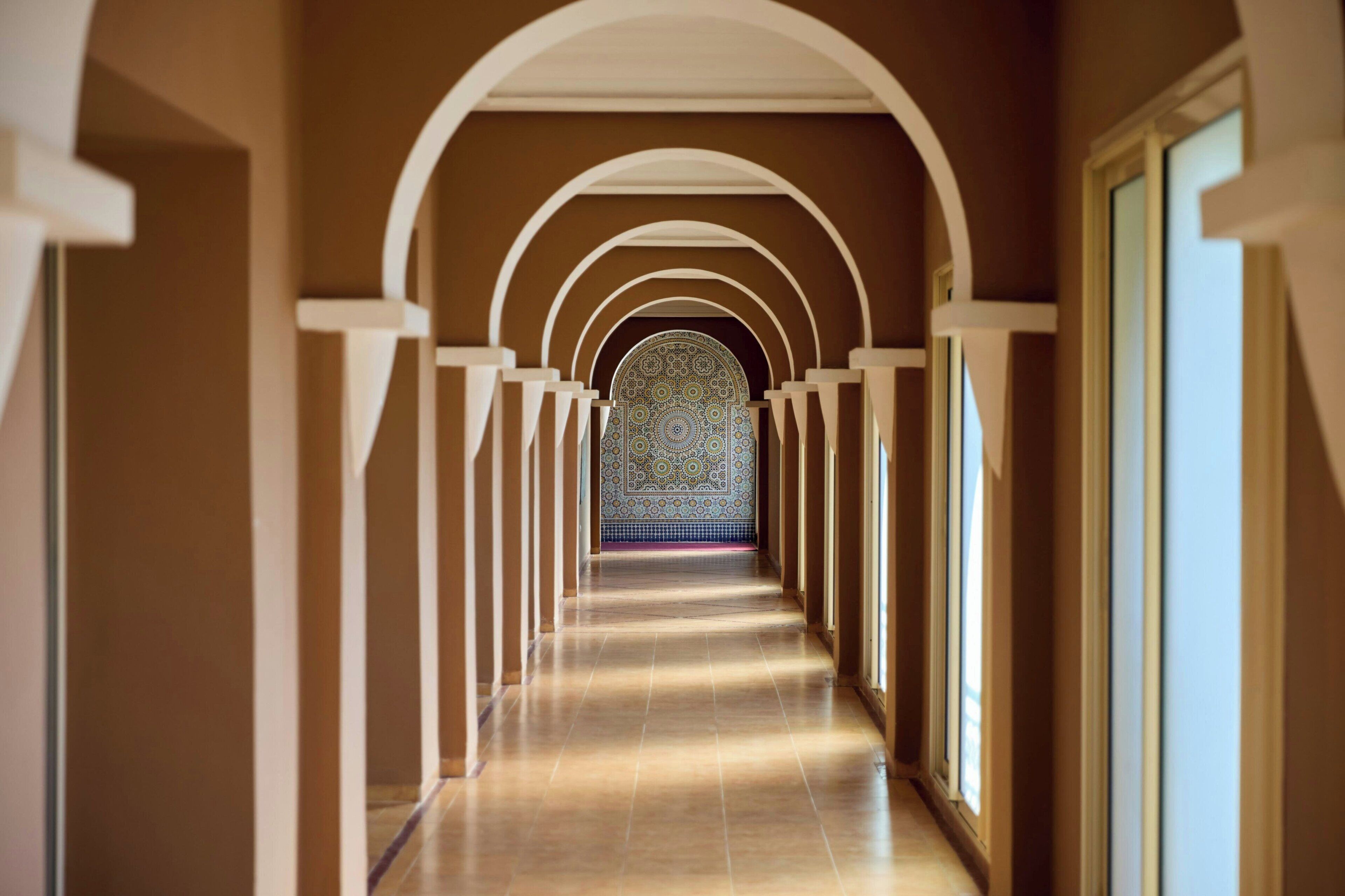 Un pasillo con arcos y un muro con diseño al final.