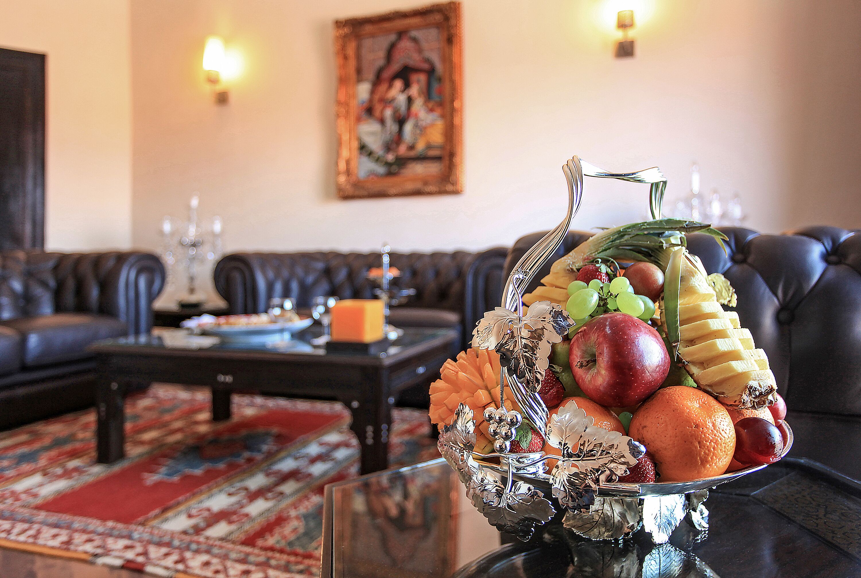Un salon avec un canapé, une table basse sur laquelle se trouve un panier de fruits, et un tableau accroché au mur.
