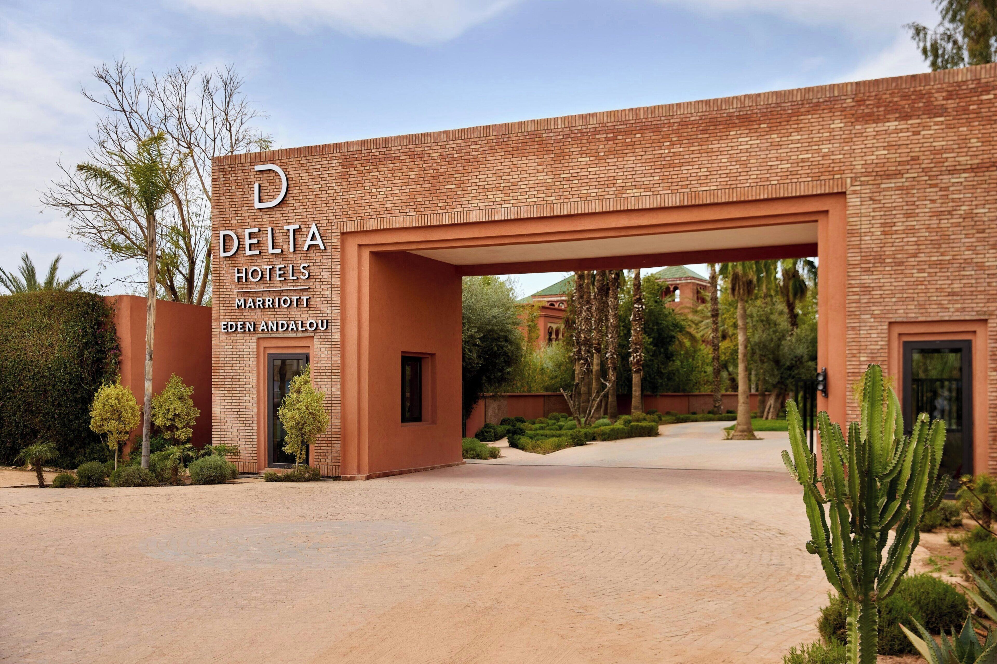 A brick building with a large archway entrance, a sign for Delta Hotels Marriott Eden Andalous, and a well-maintained garden with cacti and shrubs.