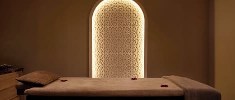 Una habitación con una cama, un banco de madera y un muro con un diseño luminoso geométrico.