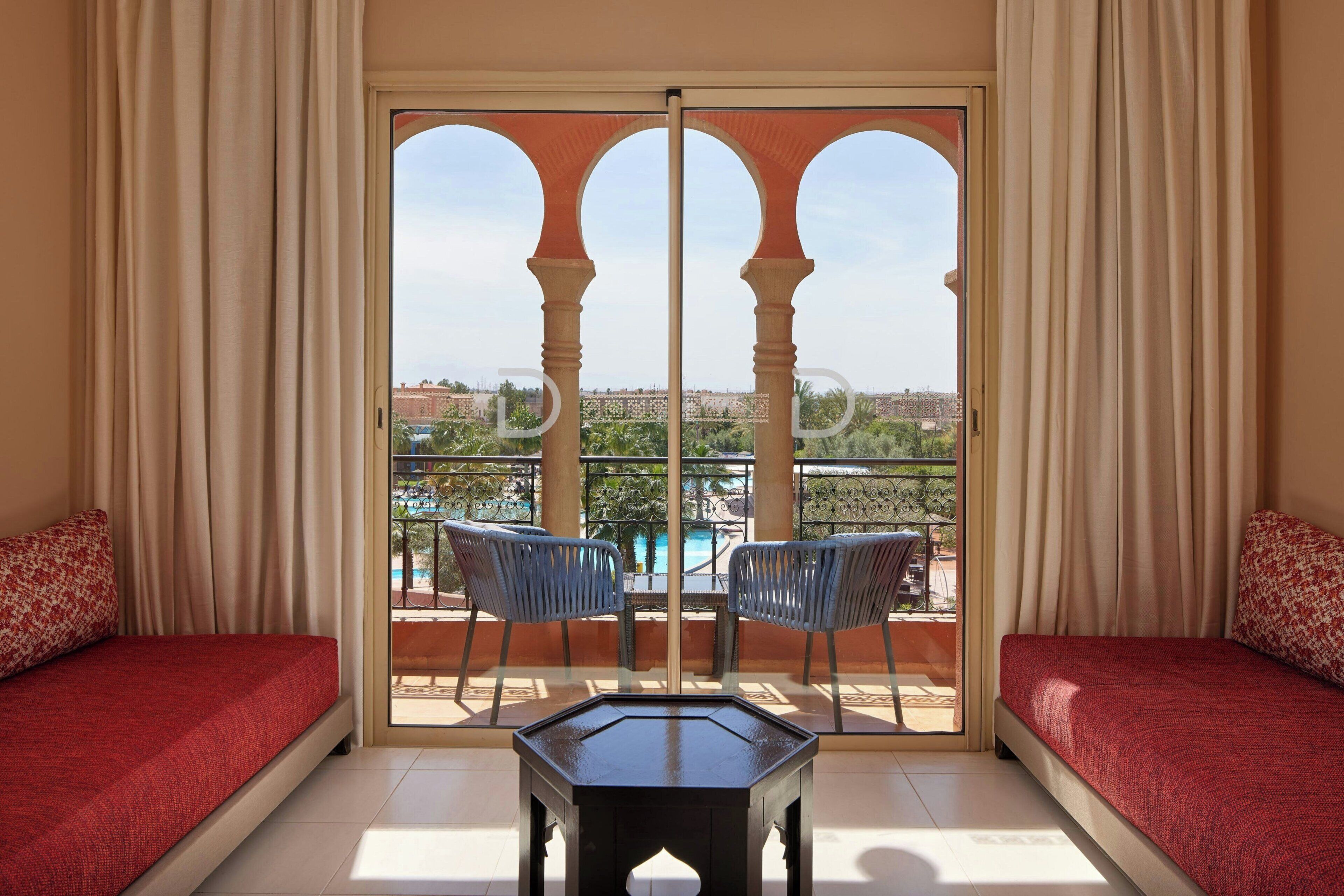 Quarto com cama, mesa e vista para a piscina e área de estar externa.