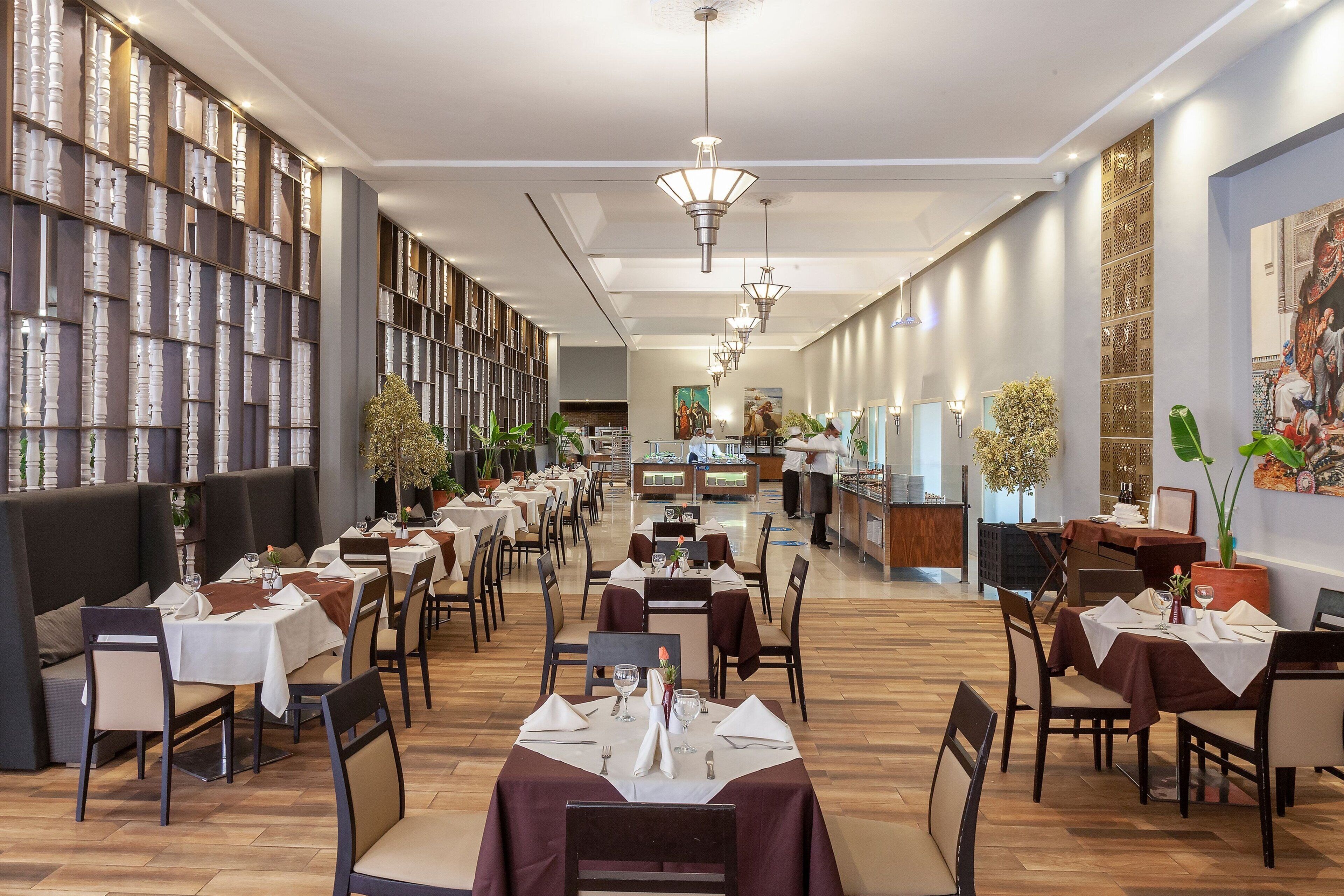 A spacious restaurant with multiple dining tables and booths, a central bar area, and decorative wall panels.