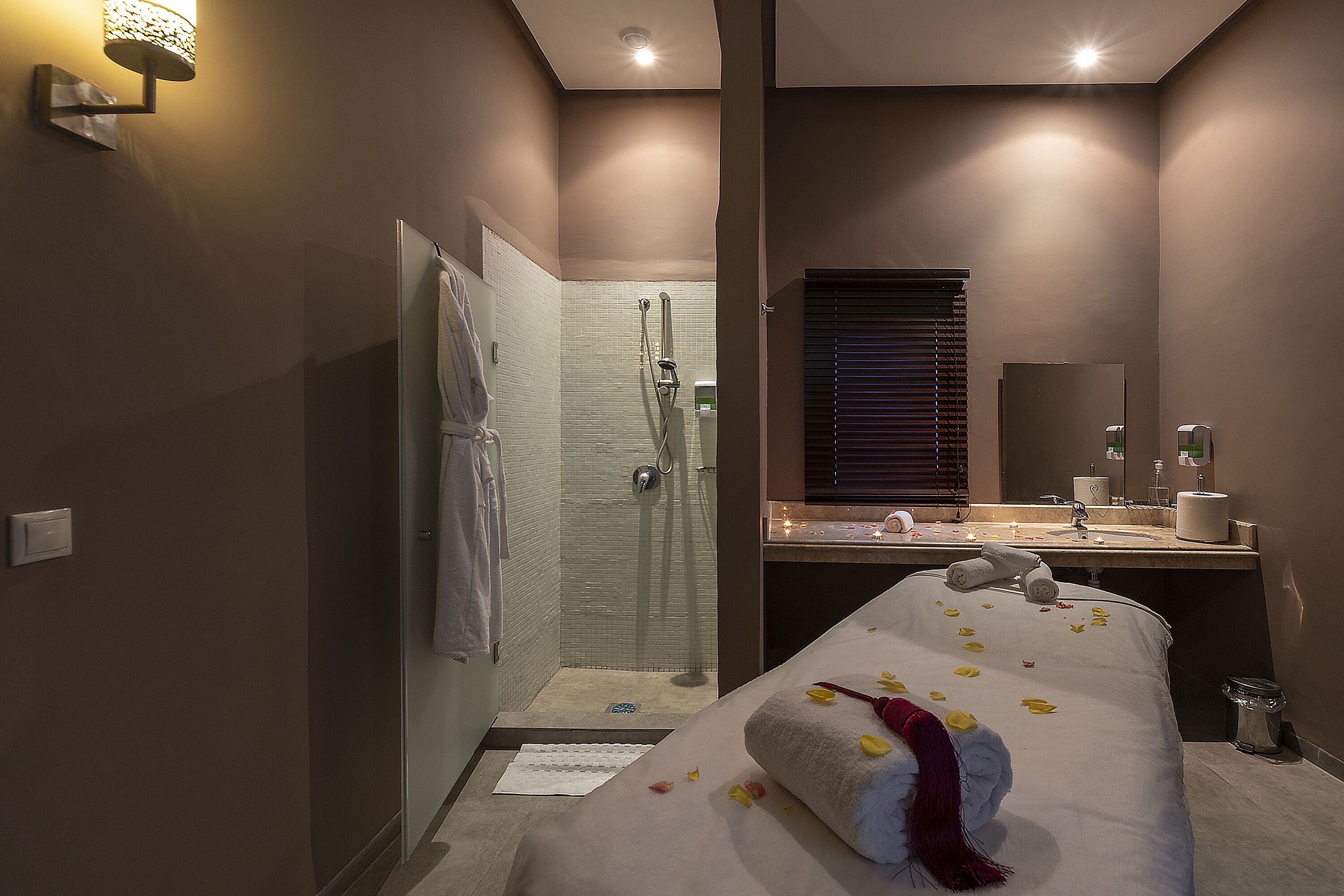 A hotel room with a shower, a bed with towels, a sink, and a mirror.