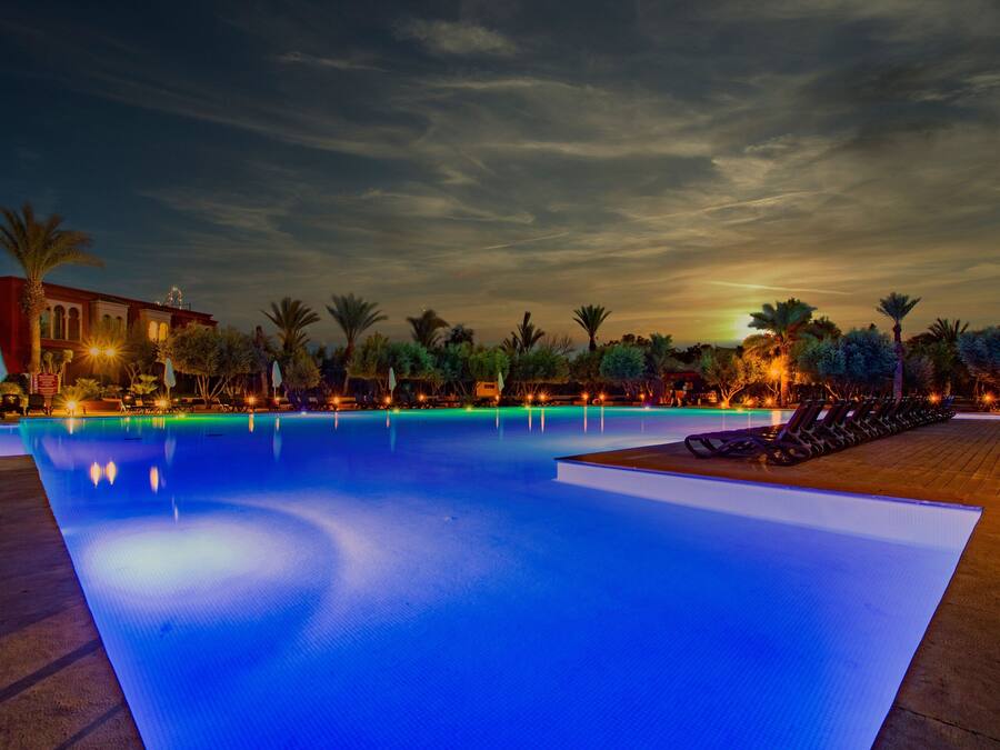 Una piscina con una vista despejada del entorno, que incluye palmeras y un edificio con ventanas arqueadas.
