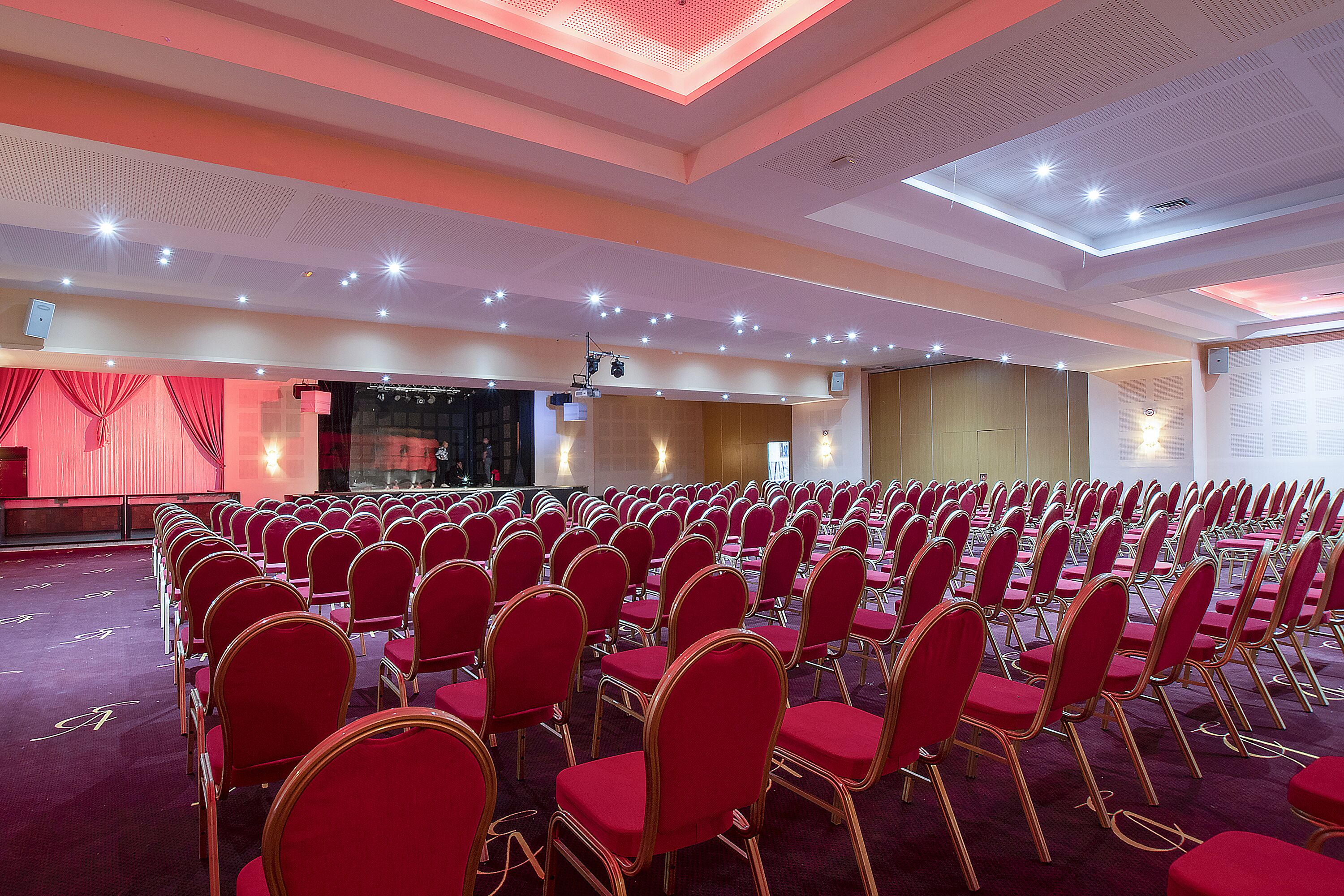 Une salle de conférence avec des rangées de chaises rouges et une scène.