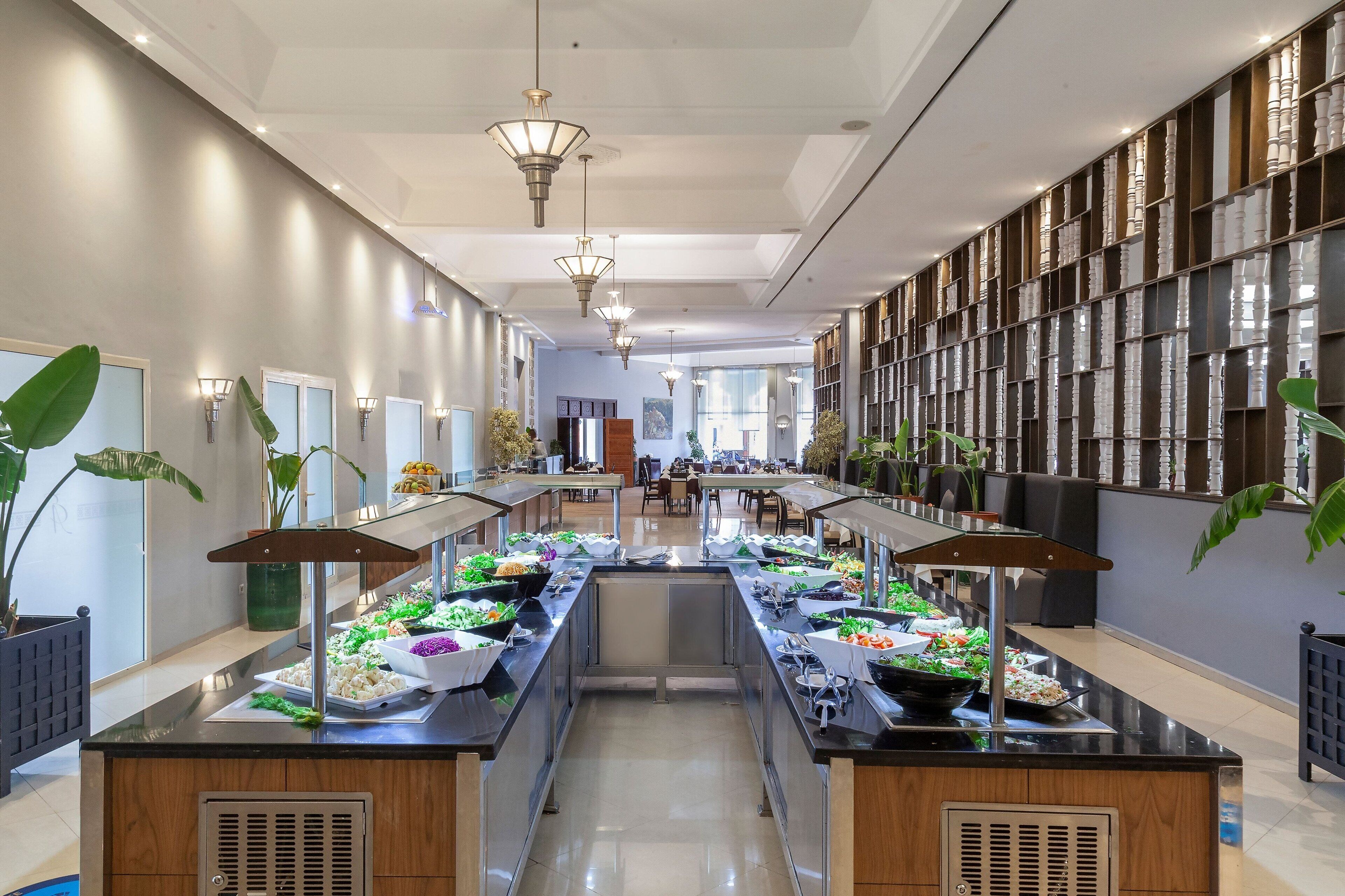 A long buffet line with various food stations, a central serving area, and a seating area with tables and chairs.
