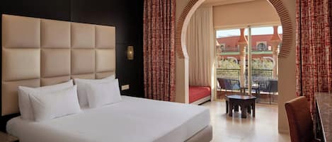 Habitación de hotel con una cama grande, un área de comedor con mesa y sillas, y un balcón con vistas.