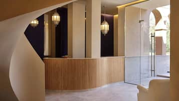 Zona de recepción con mostrador curvo de madera, faroles colgantes y puerta de cristal que da a un espacio exterior.