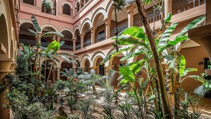 Une cour intérieure dotée de nombreuses arcades, d’une végétation luxuriante et d’un immeuble à plusieurs étages avec des balcons.