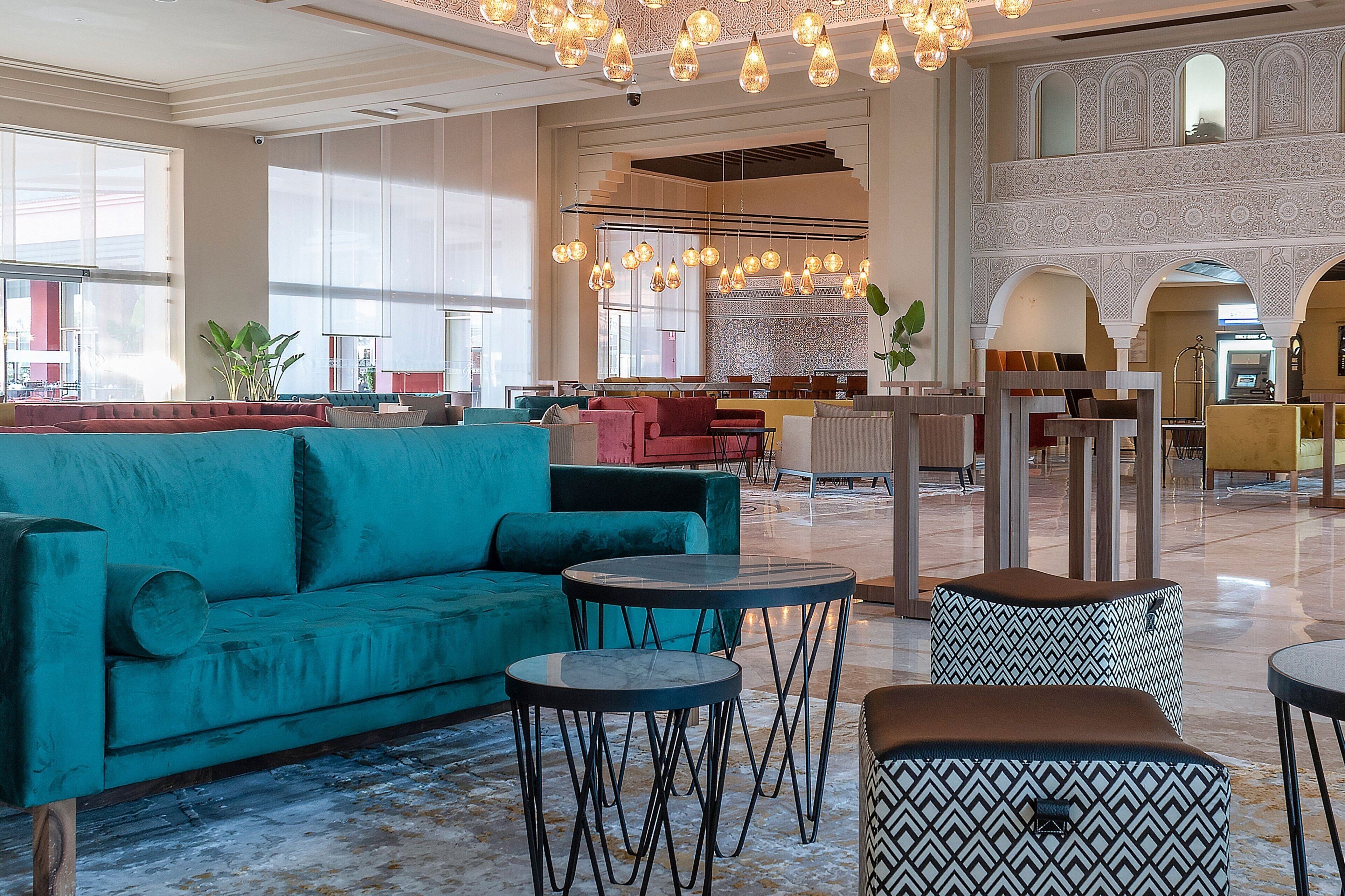 A spacious lobby with a teal sofa, round tables, and a patterned ottoman.