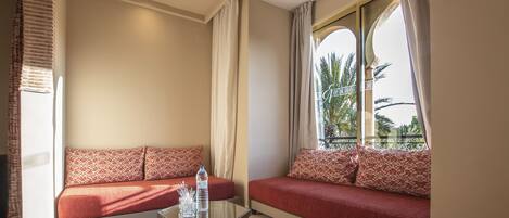 Una habitación con dos sofás rojos, una mesa de centro de cristal y vistas a palmeras a través de una ventana.