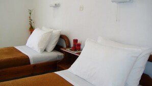 A hotel room with two beds, white bedding, a wooden headboard, a small table with a red candle, and a wall-mounted light fixture. - Rantos Apartments (Corfu)