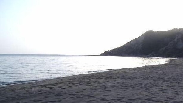 A beach with a sandy shore and a rocky cliff in the background. - Rantos Apartments (Corfu)