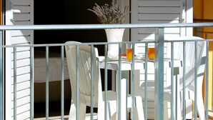 An open balcony with white chairs and a table, a potted plant, and a view into the adjacent room. - Rantos Apartments (Corfu)