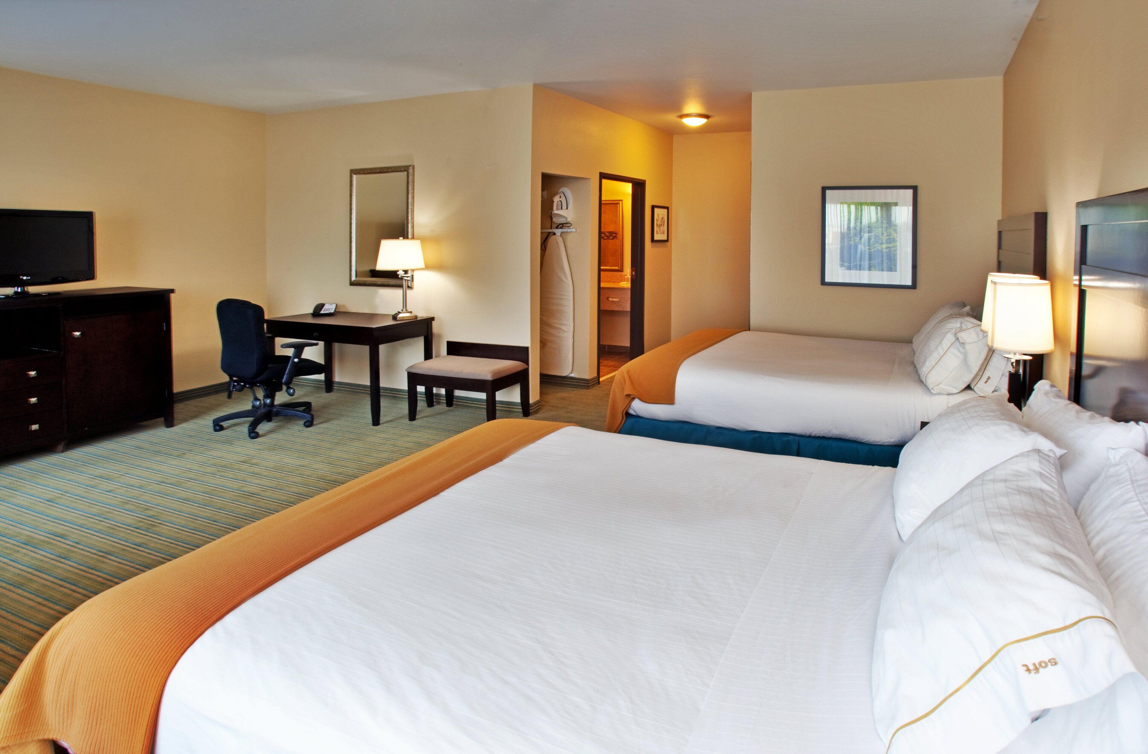 Une chambre d’hôtel avec deux lits, un bureau, une chaise, une télévision et une salle de bain visible à travers une porte ouverte.
