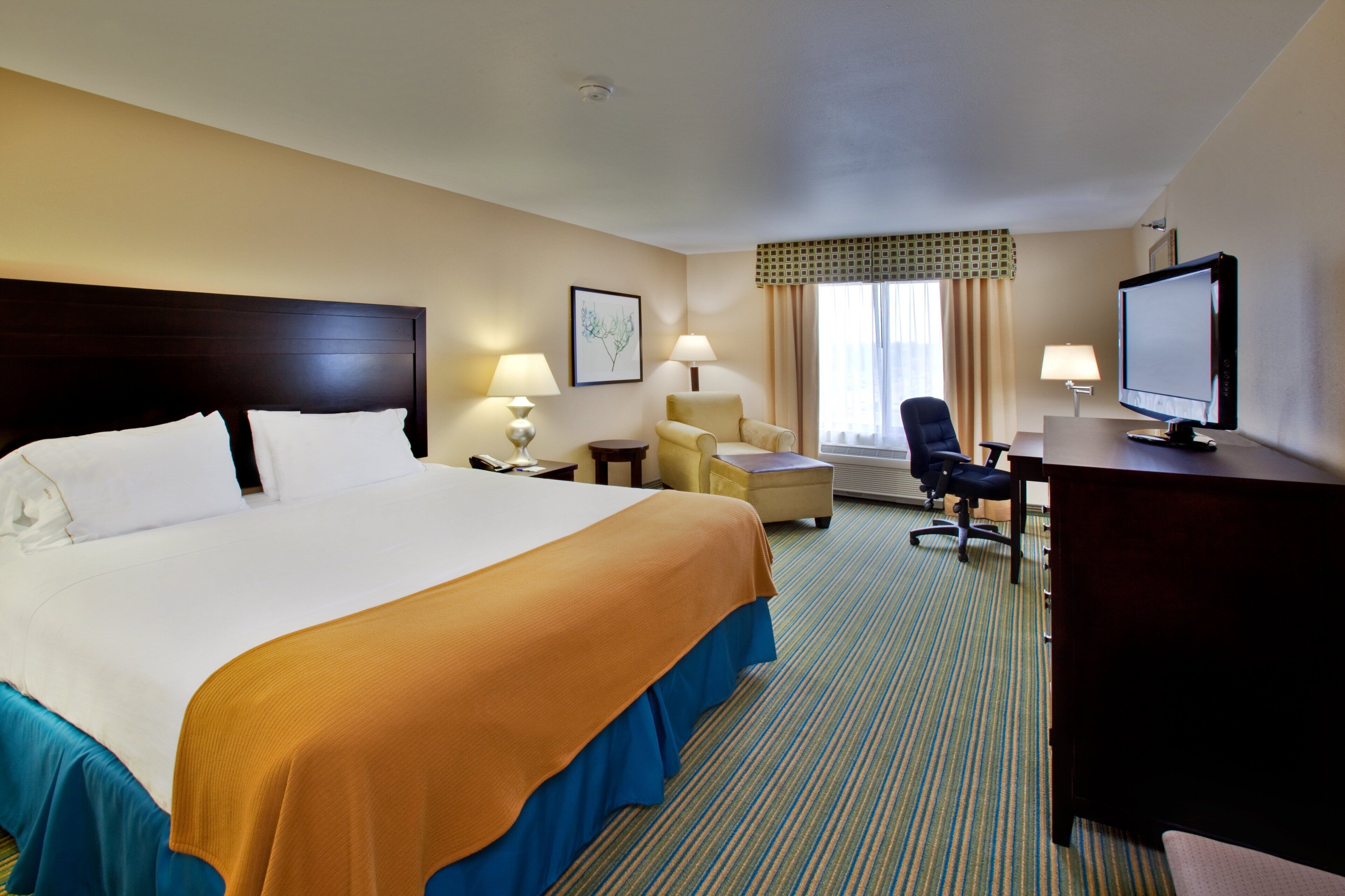 A hotel room with a large bed, a desk with a computer, a chair, and a television.