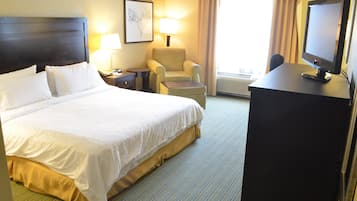 A hotel room with a large bed, a desk with a computer, a chair, a lamp, and a window with curtains.