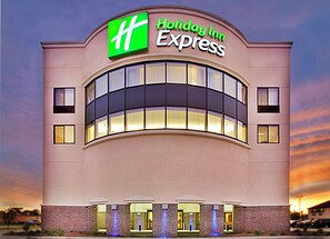 A Holiday Inn Express building with a prominent green and white logo, large windows, and a brick facade. - Holiday Inn Express Waterloo Cedar Falls by IHG (Waterloo)