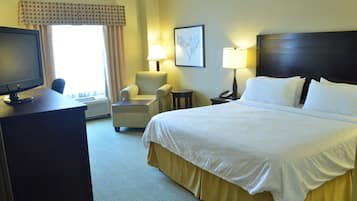 Habitación de hotel con una cama, un escritorio con computadora, una silla, dos lámparas de noche y un ventanal con cortinas.