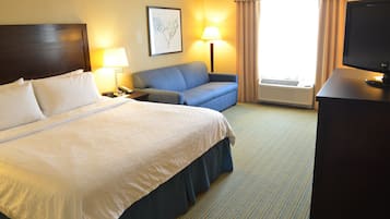 Habitación de hotel con una cama grande, un sofá, un escritorio con televisor, una lámpara y una ventana con cortinas.