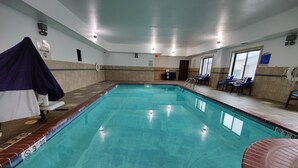 An indoor swimming pool with a tiled floor, a lifeguard chair, and a poolside area with chairs and a notice board. - Holiday Inn Express Waterloo Cedar Falls by IHG (Waterloo)