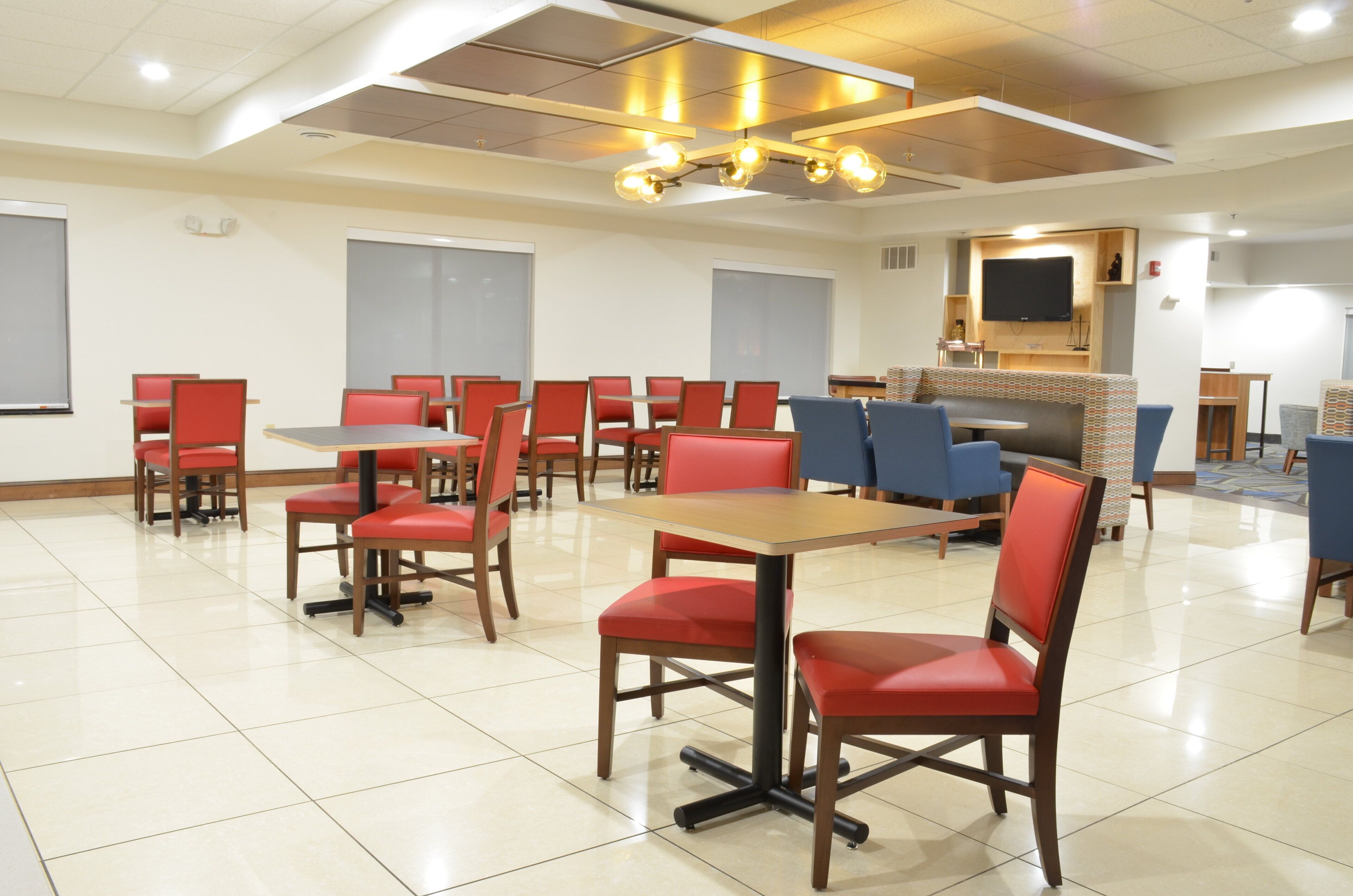 A conference room with multiple tables and chairs, a large screen, and a flat-screen TV mounted on the wall.