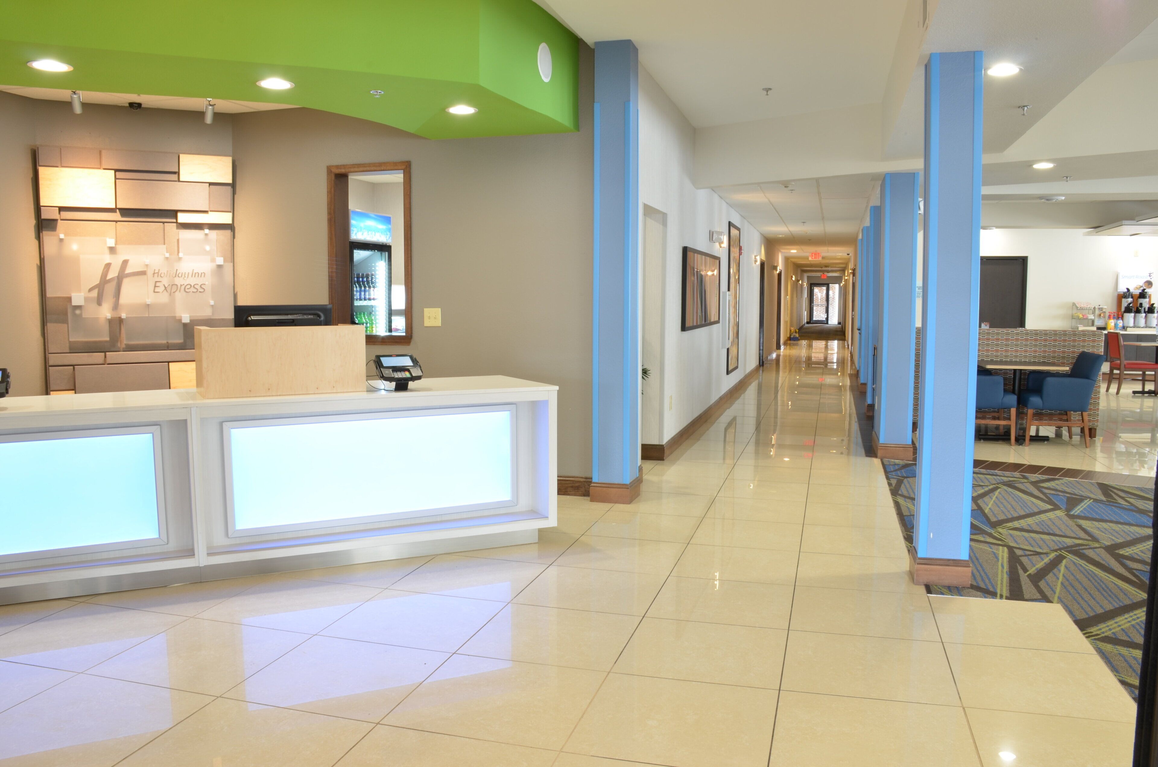 Zona de recepció d'hotel amb mostrador, nevera i espai d'estar amb taules i cadires.