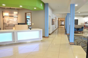 A hotel reception area with a counter, a refrigerator, and a seating area with tables and chairs.