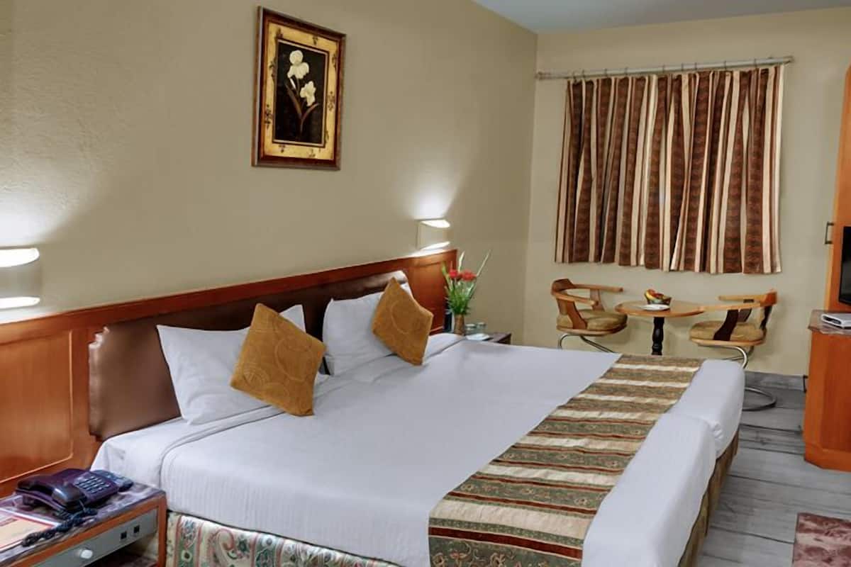 A hotel room with a large bed, a desk with a TV, a small table, and a chair.