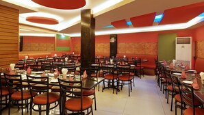 Un restaurante con varias mesas y sillas, paredes rojas y verdes, y un diseño moderno en el techo.