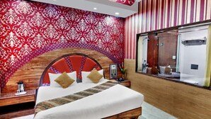 Habitación de hotel con una cama grande, cabecero de madera, un espejo y ventana con vista al baño.