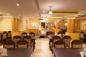 Comedor de hotel con varias mesas y sillas, una estación de lavado de manos y vista al área de cocina.