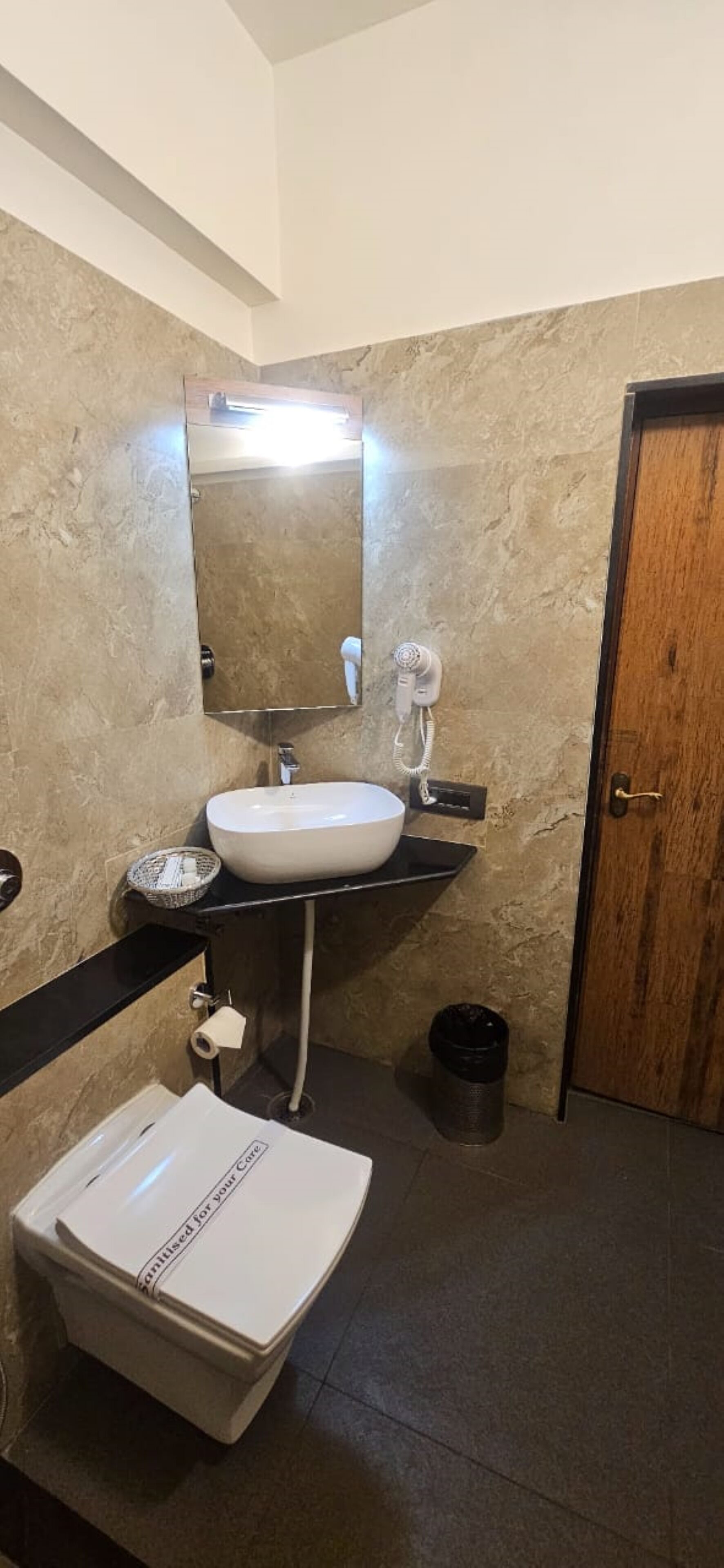 A bathroom with a white sink, a mirror, a towel rack, a trash can, and a toilet paper holder.