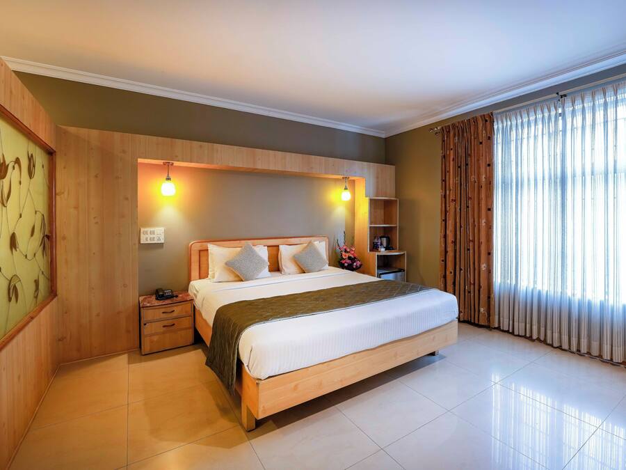 A hotel room with a wooden bed, a nightstand, a shelf with toiletries, and a large window with curtains.