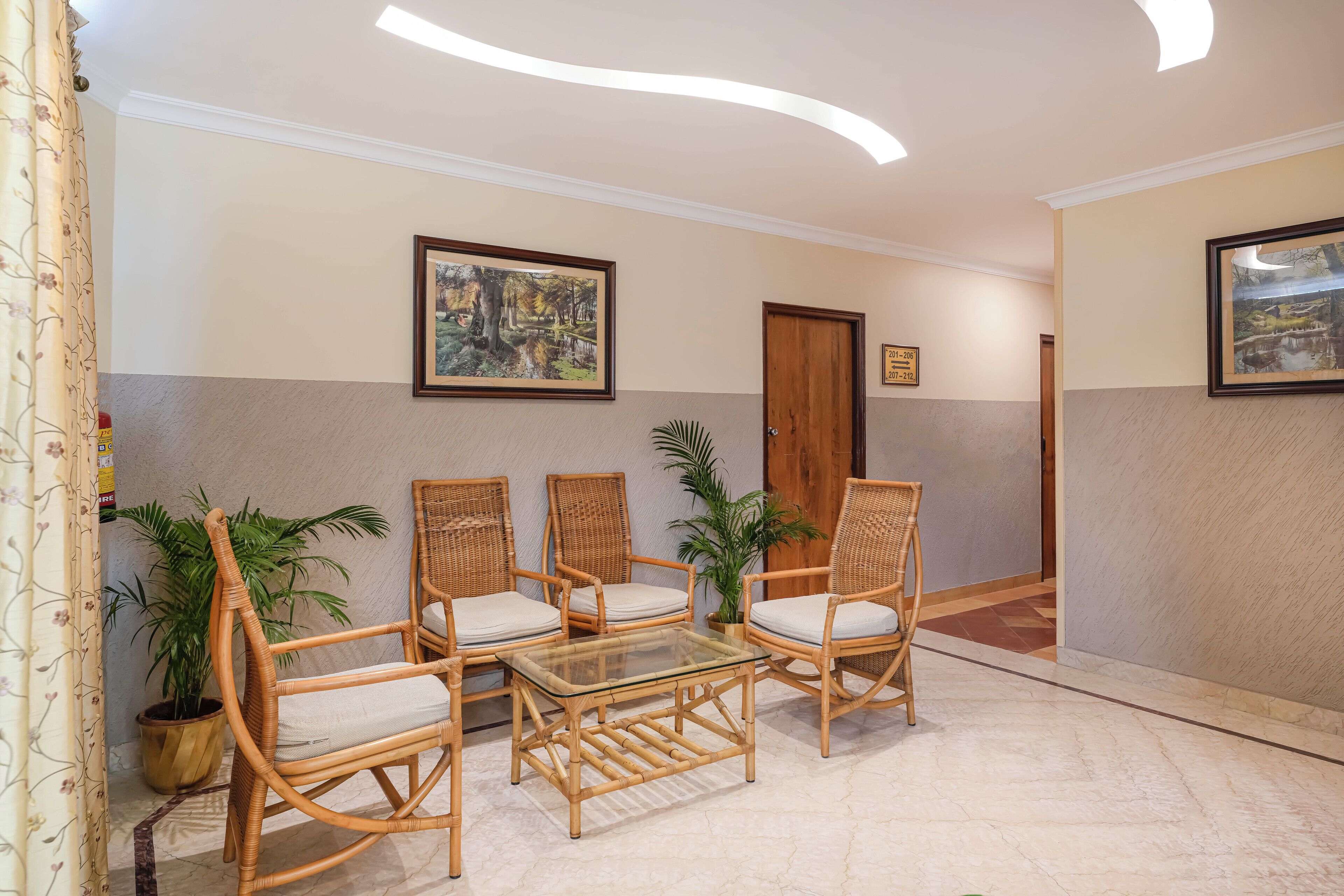 A lobby with wicker furniture, a glass-top table, and potted plants.