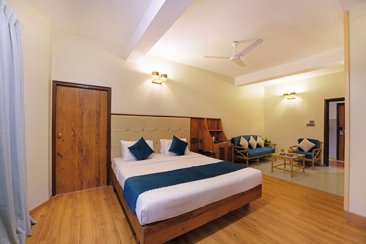 A hotel room with a wooden bed, a ceiling fan, and two seating areas with chairs and a table.