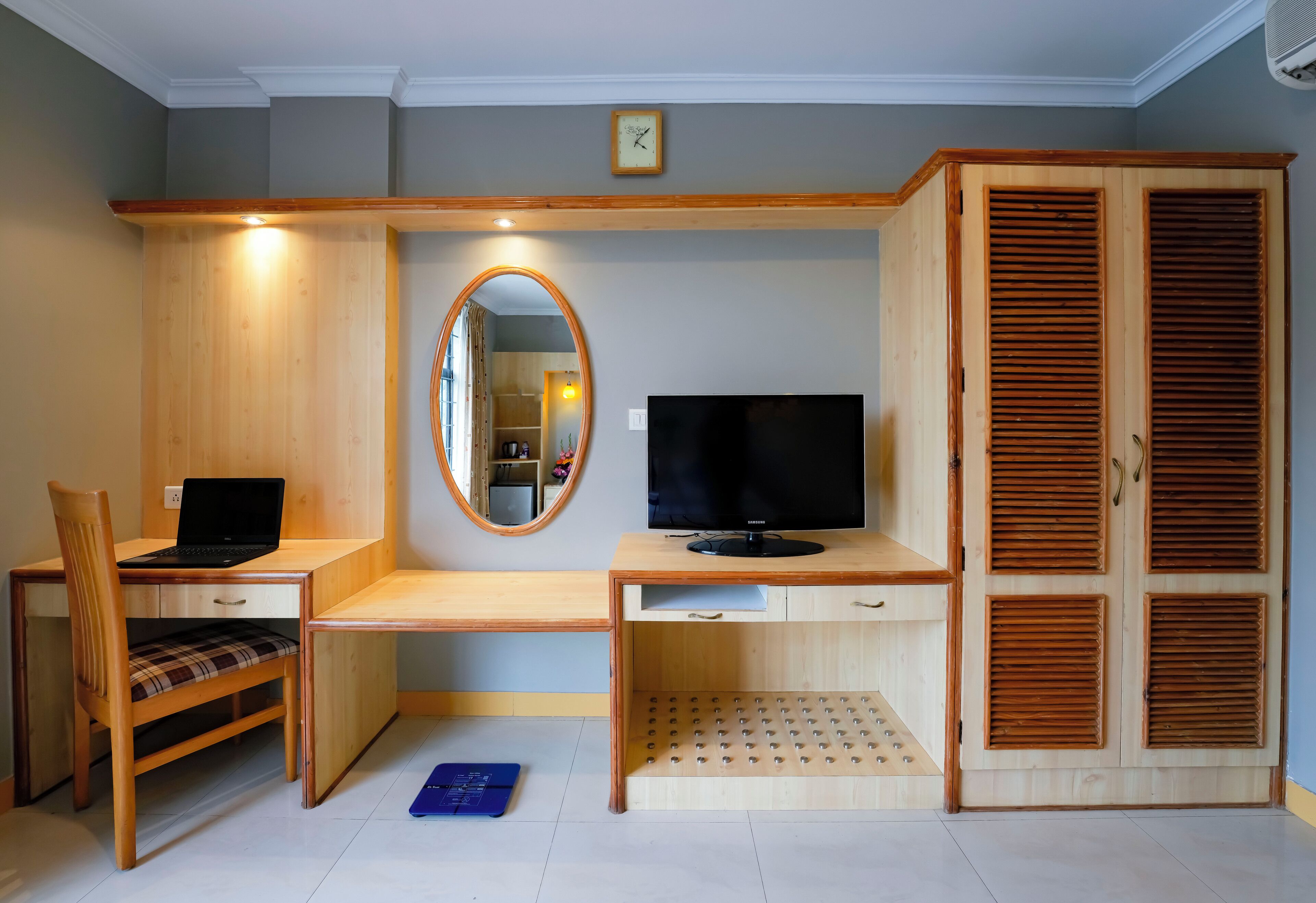 Una habitación con un escritorio de madera, una silla, un televisor, un espejo y un armario.