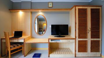 Una habitación con un escritorio de madera, una silla, un televisor, un espejo y un armario.