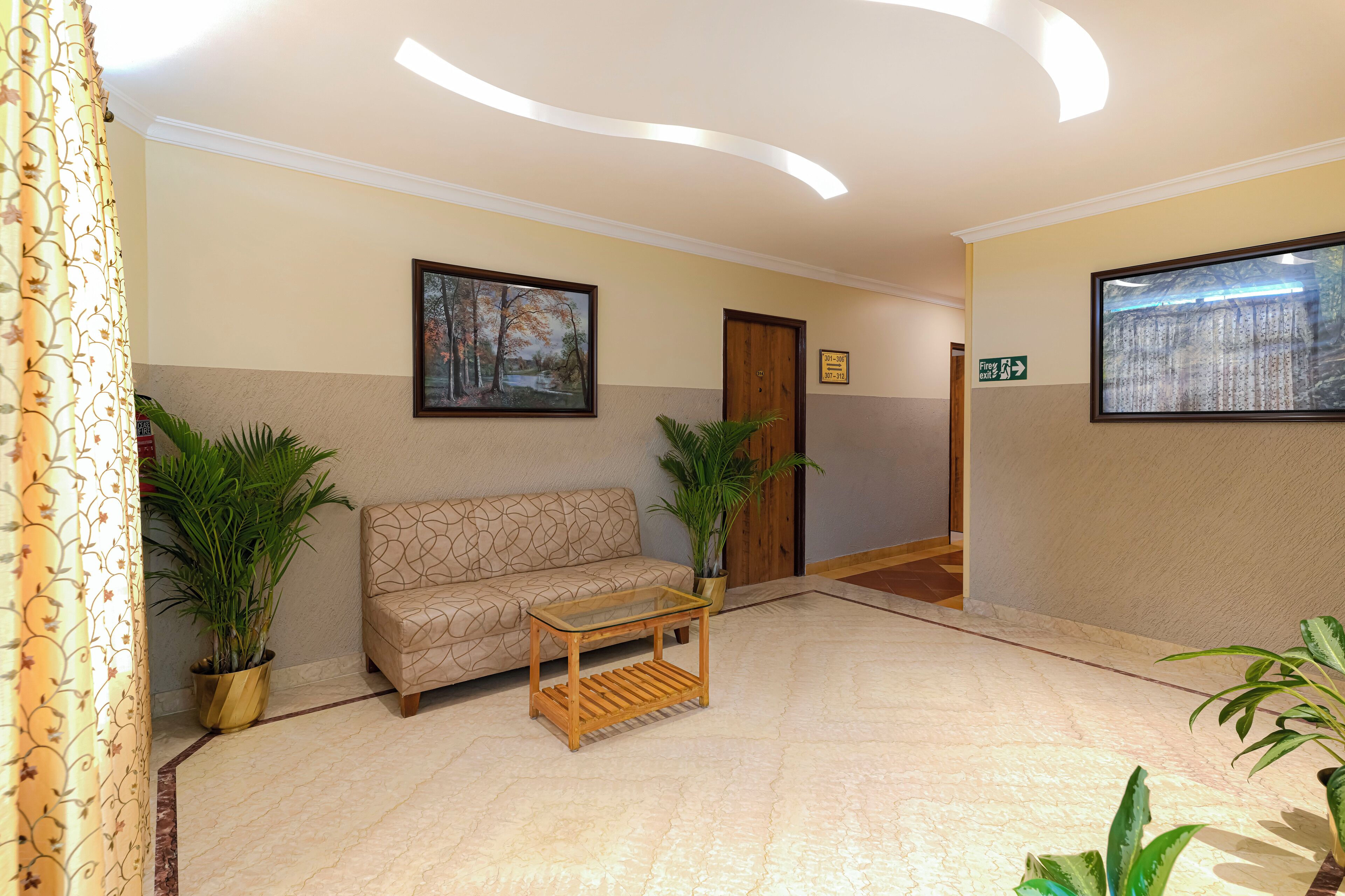 A lobby with a sofa, a glass-top table, potted plants, and a framed picture on the wall.