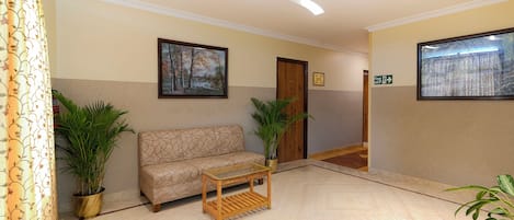 Un hall con un sofá, una mesa de vidrio, plantas en macetas y un cuadro en la pared.