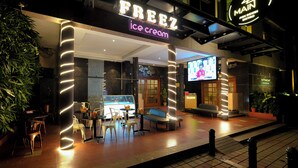 An ice cream shop named "FREEZ" with a neon sign, outdoor seating area, and a TV screen displaying a program. - Cross Roads Inn (Bengaluru)