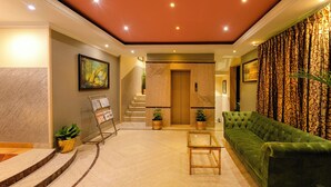 A lobby with a green sofa, a wooden coffee table, a staircase, and a painting on the wall. - Cross Roads Inn (Bengaluru)