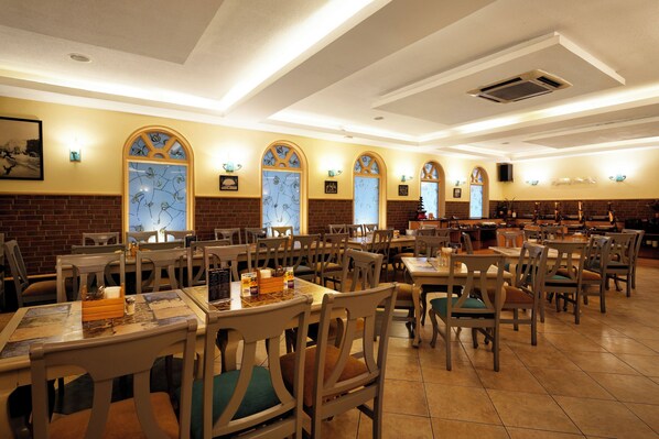 A spacious restaurant with multiple dining tables and chairs, arched windows, and a brick wall. - Cross Roads Inn (Bengaluru)