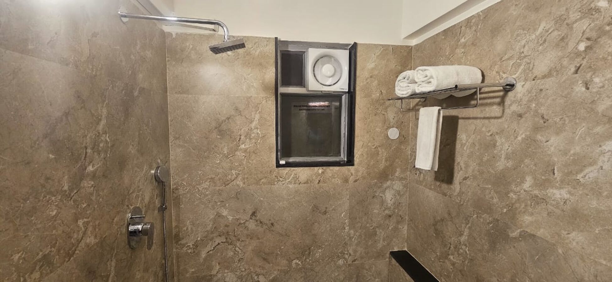 A shower with a handheld showerhead, a glass-enclosed ventilation unit, and a towel rack with towels.