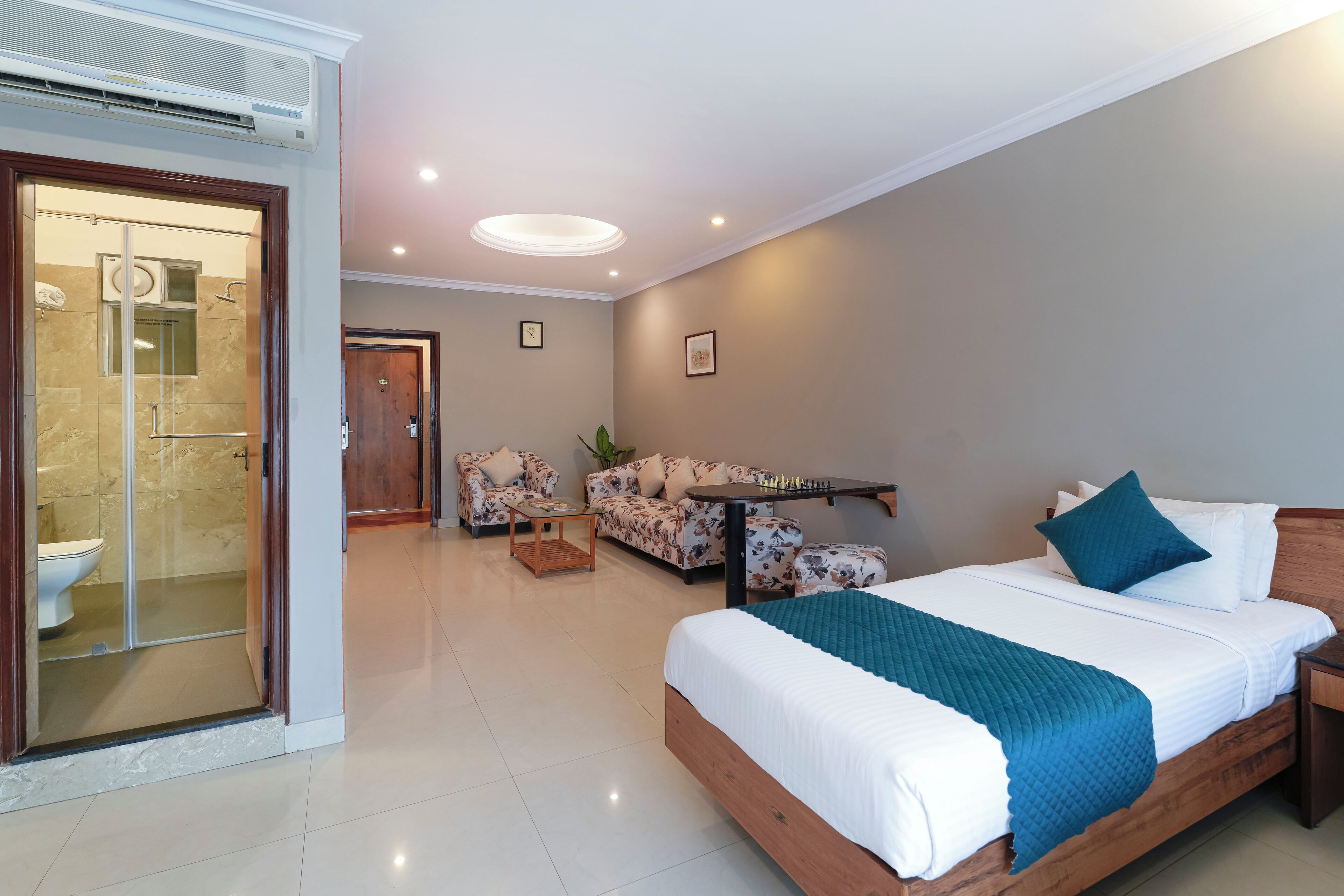 A modern hotel room with a large bed, a sofa, a small table, and a shower area.