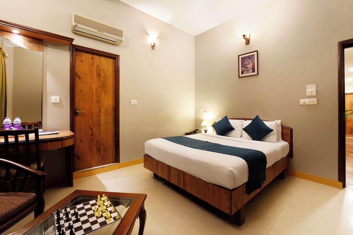 A hotel room with a wooden bed, a desk with a chessboard, a mirror, and a door.