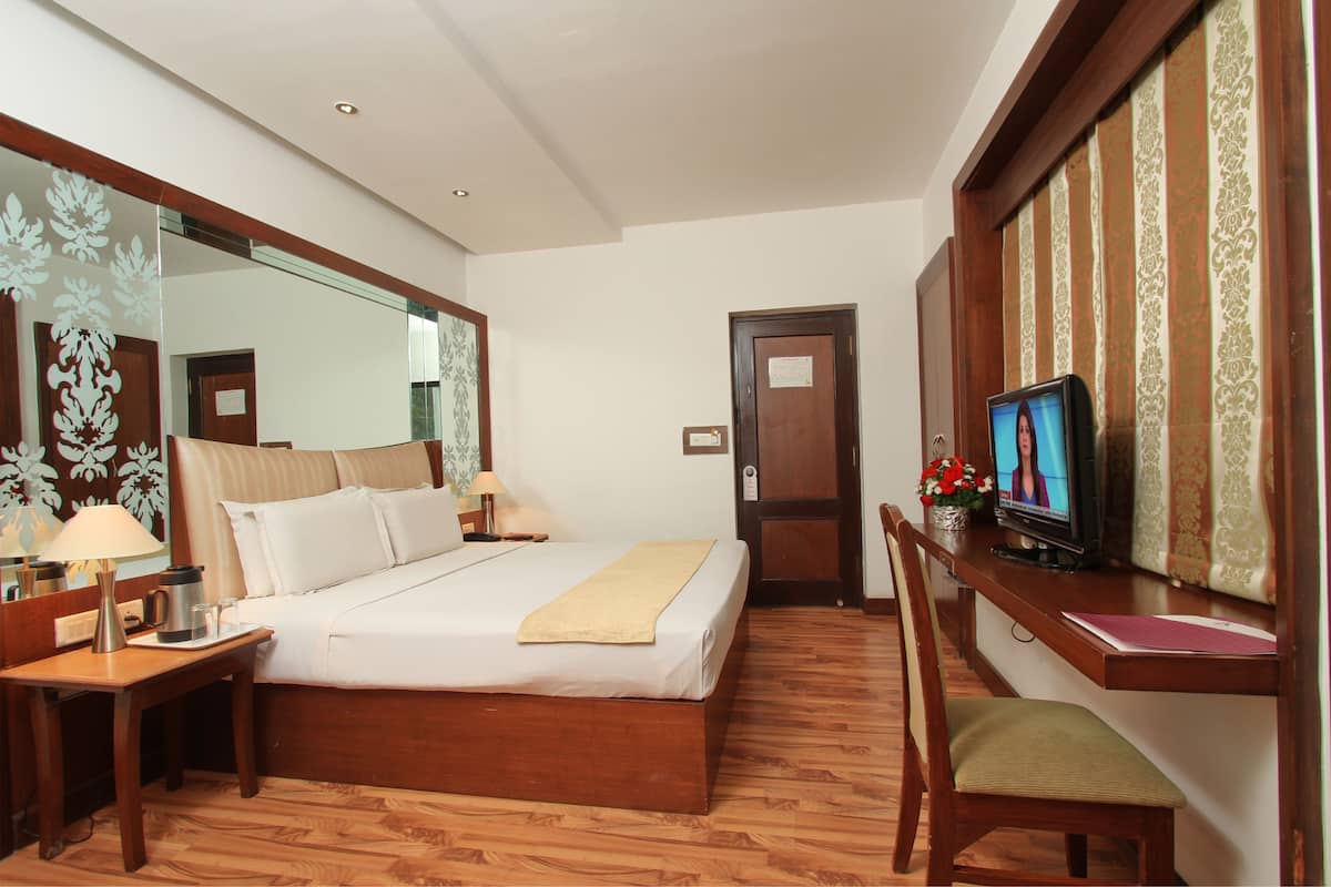 A hotel room with a large bed, a desk with a computer, a chair, and a TV.