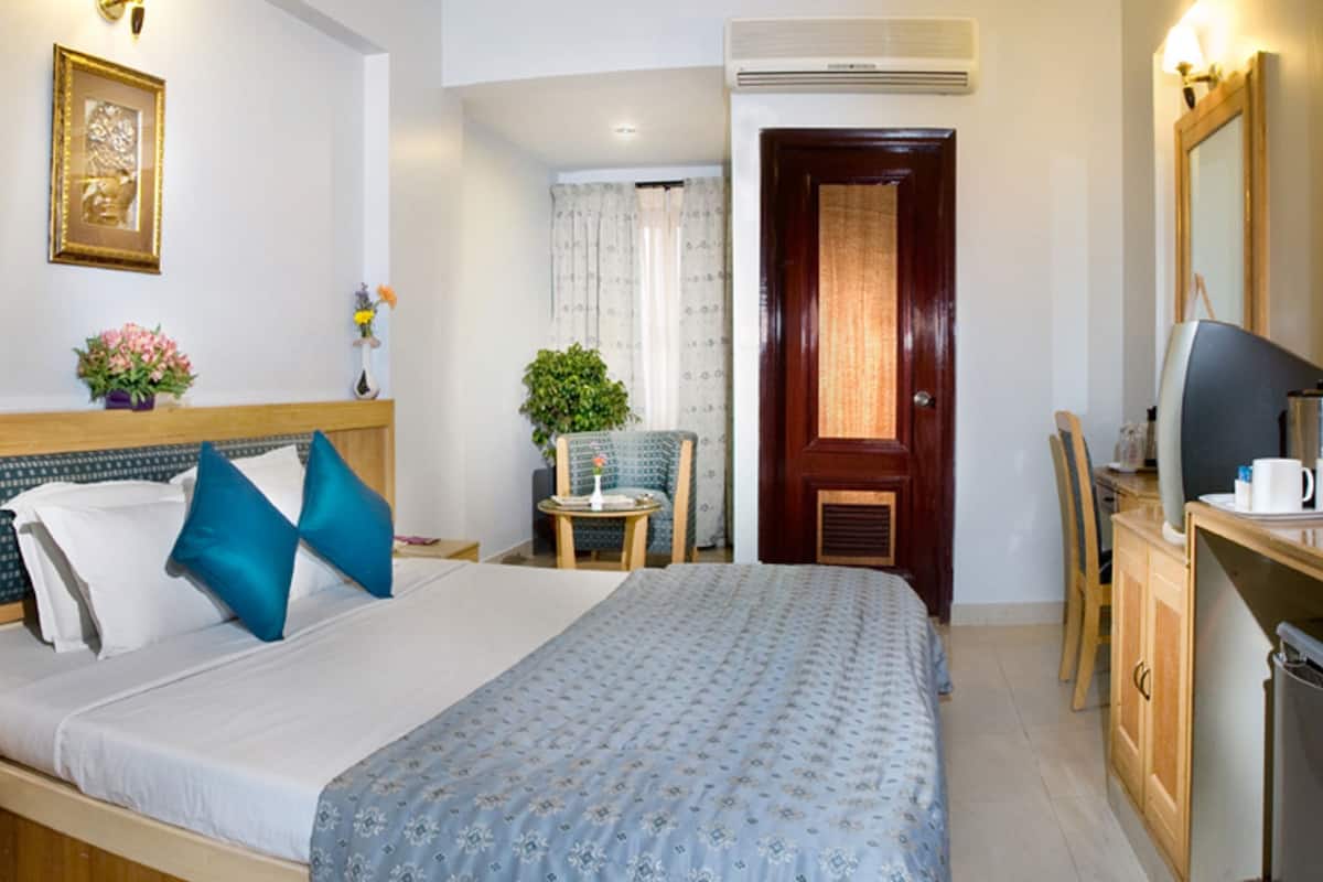 A hotel room with a bed, bedside table, TV, and a desk with a chair.