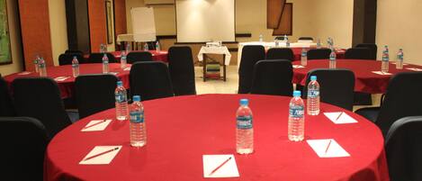 Un salón de conferencias con varias mesas cubiertas con manteles rojos, cada una con botellas de agua y blocs de notas.